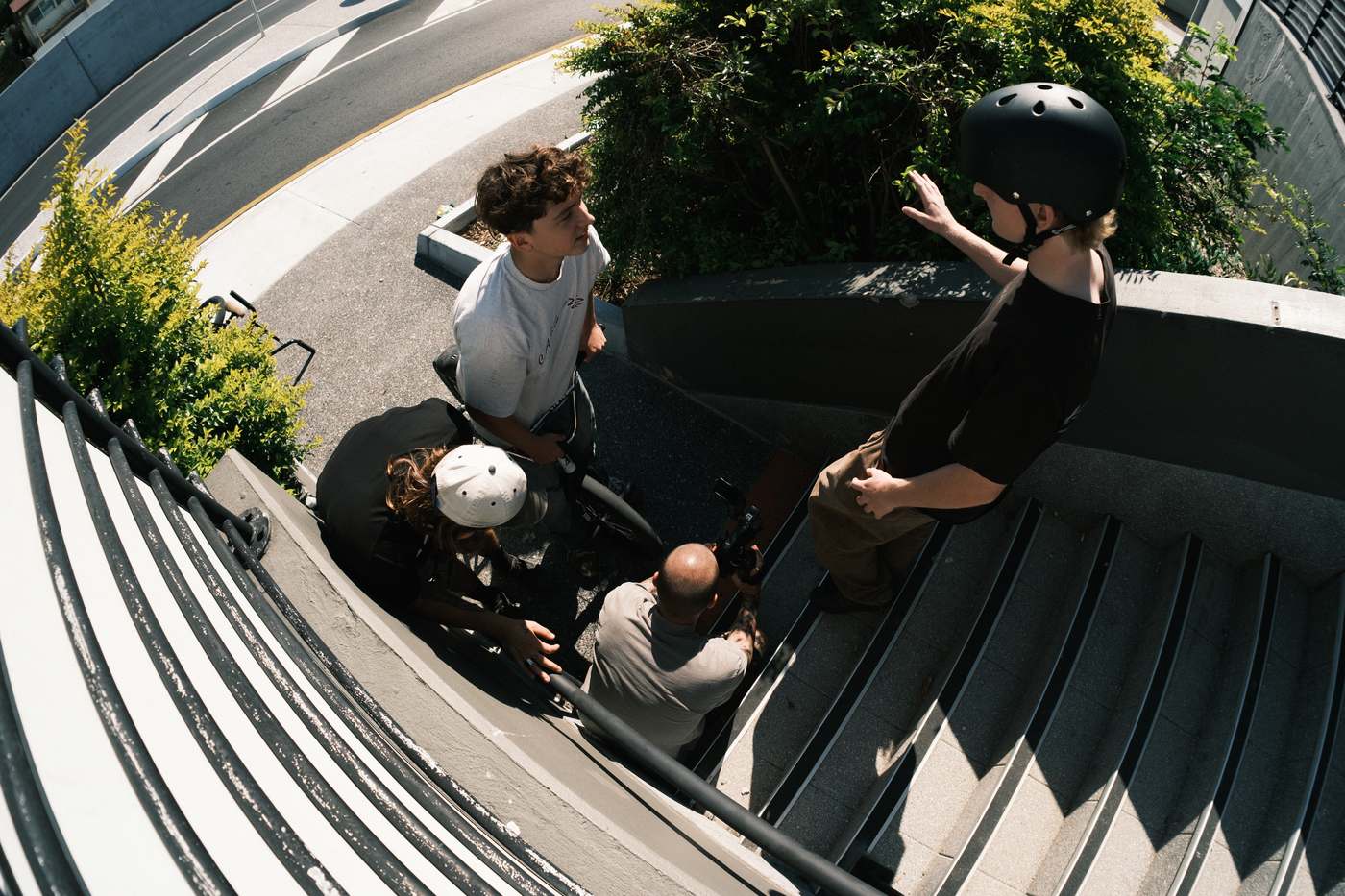 Kai on his bike at the bottom of a stairset, high fiving a rider in a helmet, the crew and a filmer gathered around.