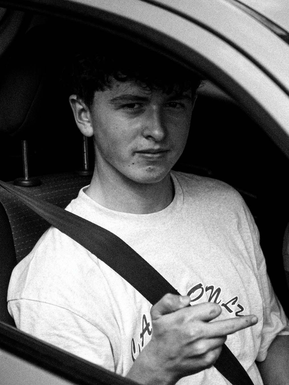 Kai in the driver's seat of a car, seatbelt on, window down, in black and white.