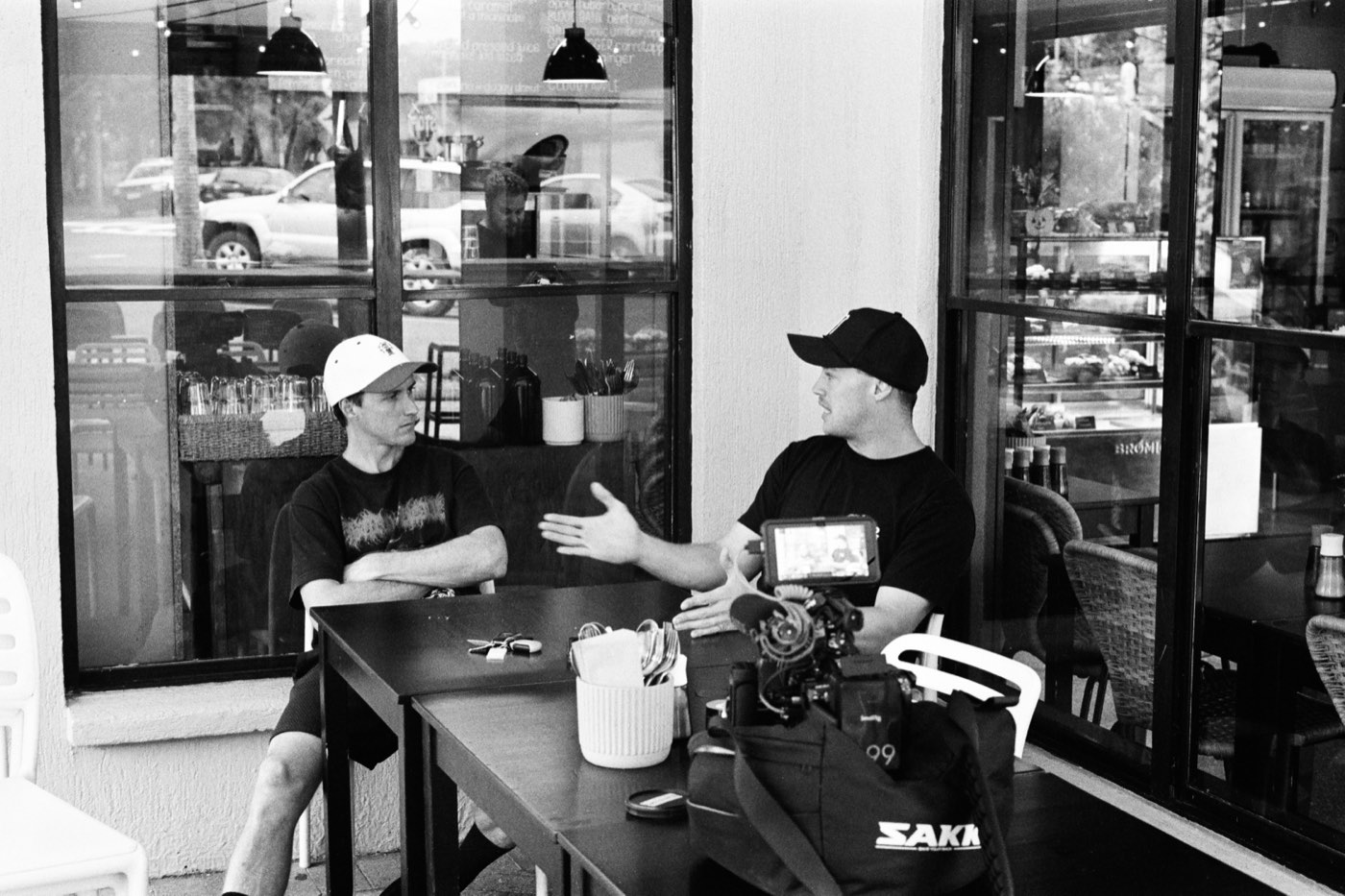 Ryan and Mike talking across a cafe table, a camera on the table between them.