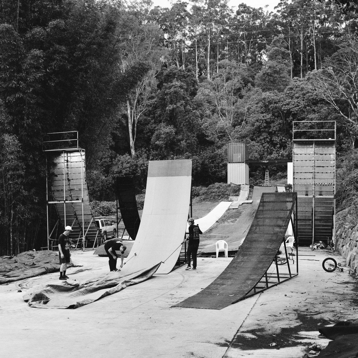 A row of ramps of increasing size in a forest clearing, two people pulling a tarp off the smallest.
