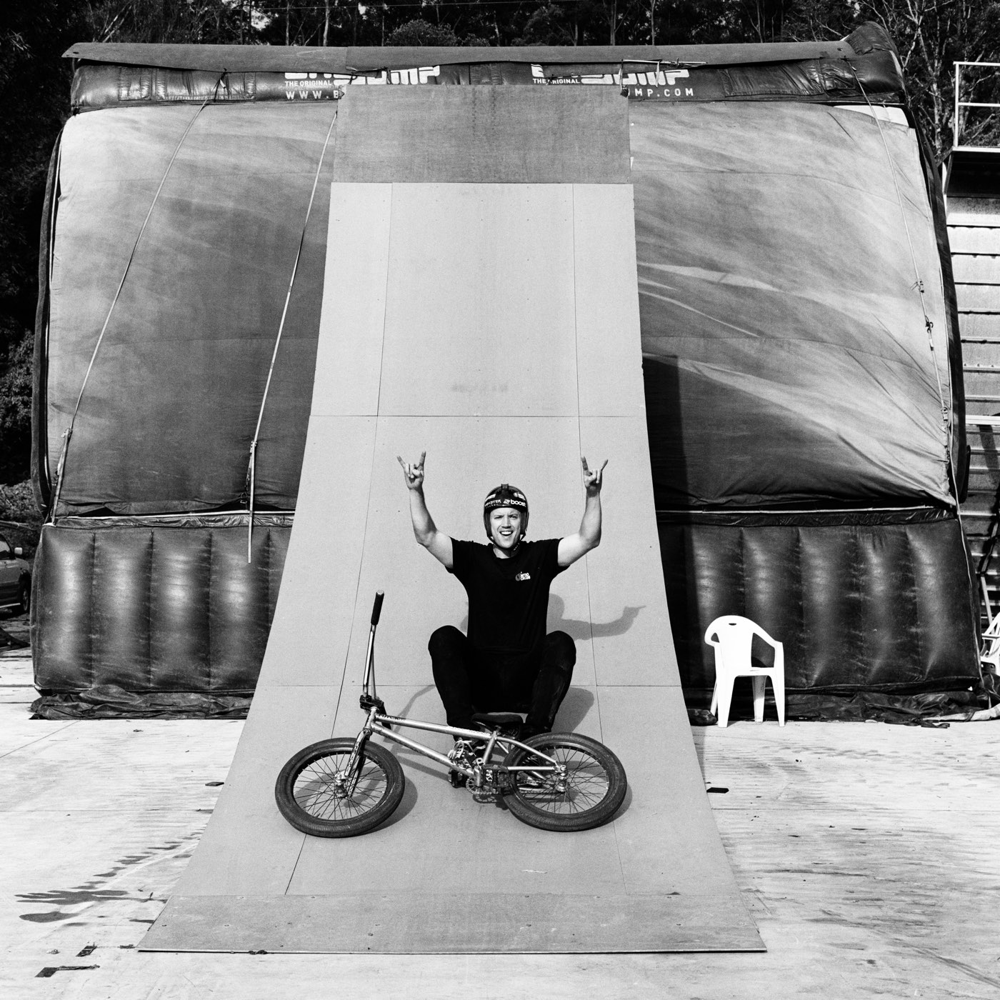 Ryan sitting at the top of a quarter pipe with both arms raised, bike at the bottom.