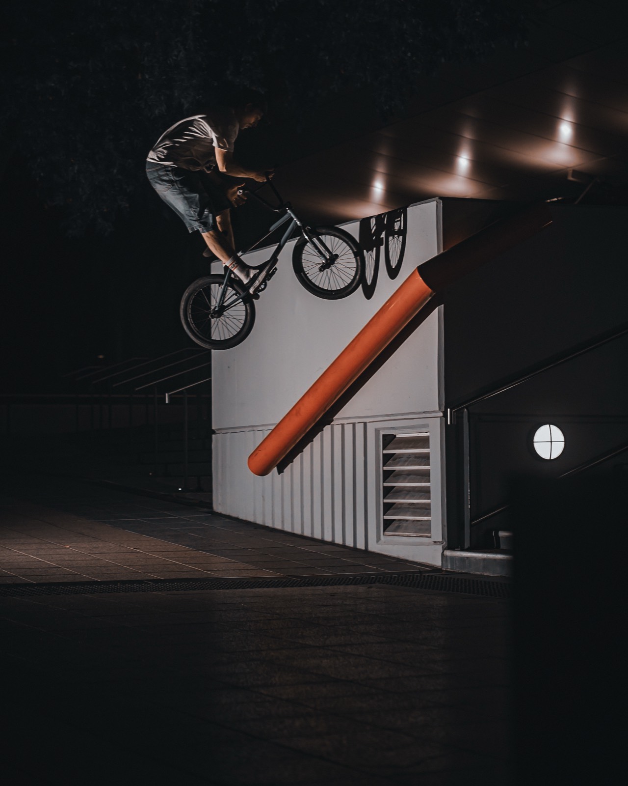 Renato Rancso turning a bars 180 off a white wall at night, an orange pole angled across the frame.