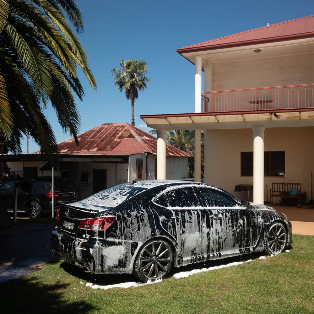 Album cover for Trek by Shady Nasty: a dark sedan covered in soap suds parked on a lawn in front of a two-storey house and palm trees.